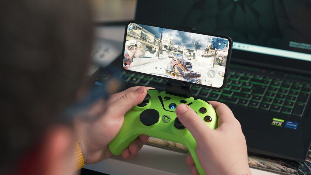 Close view of hands on a green controller and smartphone screen showing game that creates immersive gameplay.]