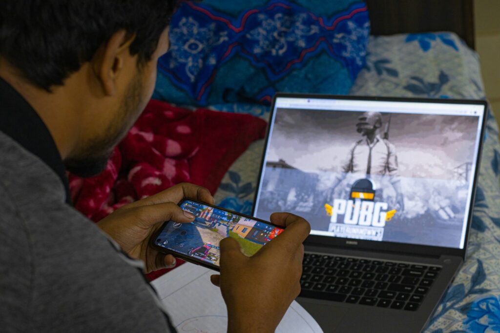 A gamer playing a localized version of gameplay on mobile and laptop.