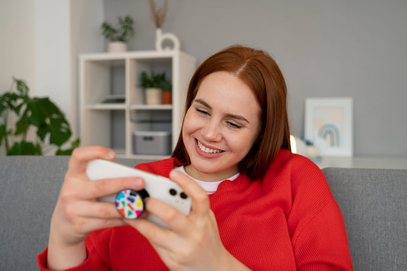 A woman relaxing on a couch while playing a mobile game on her phone.