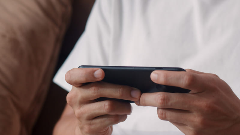 A gamer is holding a smartphone and playing a localized mobile game.