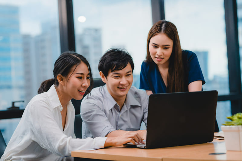 A group of professionals gathers around a laptop, working on strategic localization support for a mobile game.