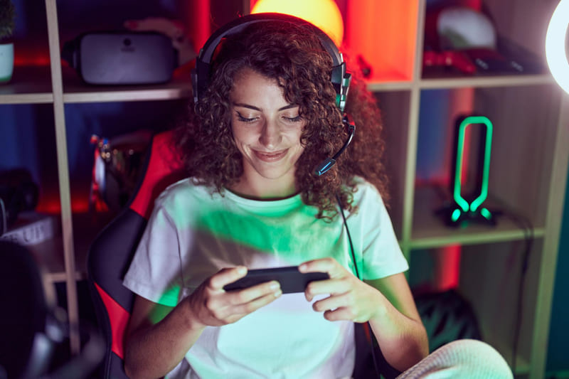 A female gamer sitting in a chair immersed in a mobile simulator game on her phone.