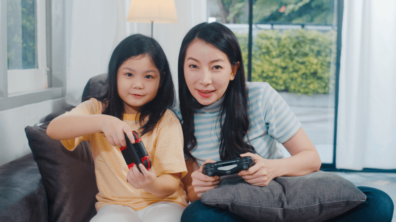 A Southeast Asian mother and daughter are casually playing a video game in their home.