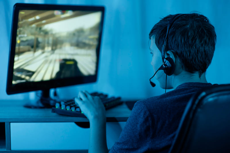 A young gamer at a desktop computer playing games across multiple modern genres.