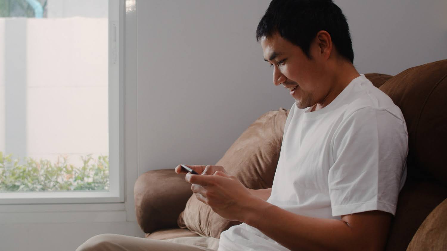 An Indonesian gamer smiling while playing an online game on a smartphone