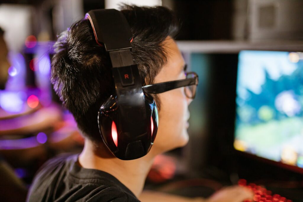 An Indonesian gamer wears headphones while playing a video game on a PC.