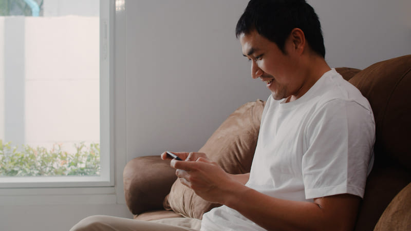 An Indonesian gamer smiling while playing an online game on a smartphone.