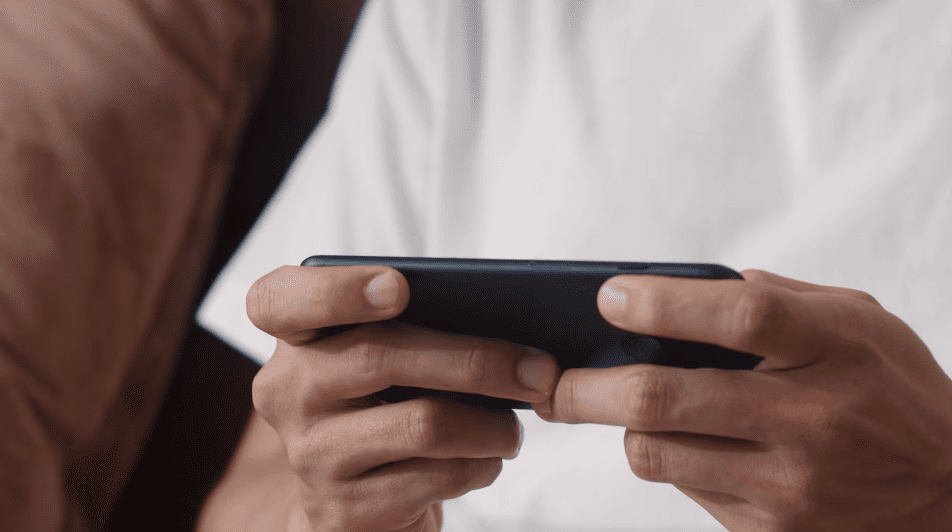 Close-up view of hands holding a dark smartphone horizontally in a mobile gaming grip.