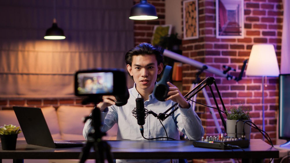 A male Southeast Asian gaming content creator reviewing headphones on camera in a professional studio setup, illustrating creator-led game discovery.