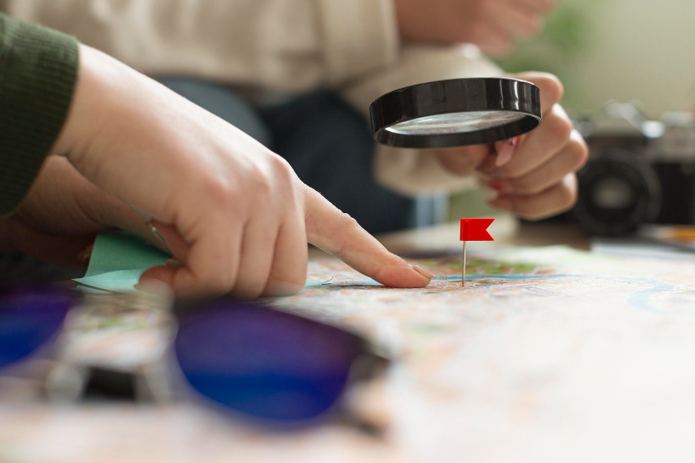 A close-up of hands using a magnifying glass over a map with a red pin, symbolizing precise localization quality assurance (LQA) inspection.