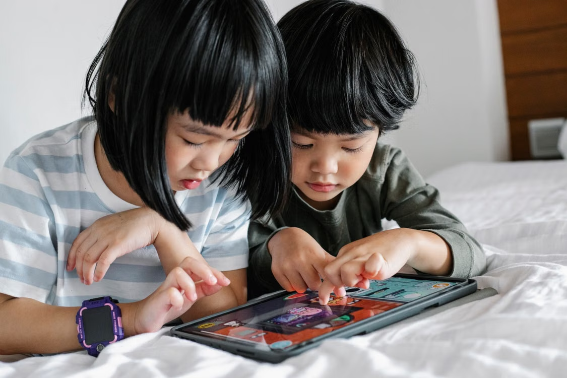 Two Indonesian children enjoying a game together on a tablet.  
