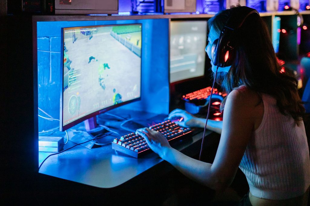 A woman wearing a headset and playing a PC game in a vibrant, neon-lit gaming setup.