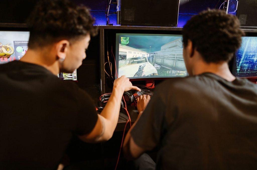 A gamer pointing at a first-person shooter game display filled with UI text, timers, and radar indicators.