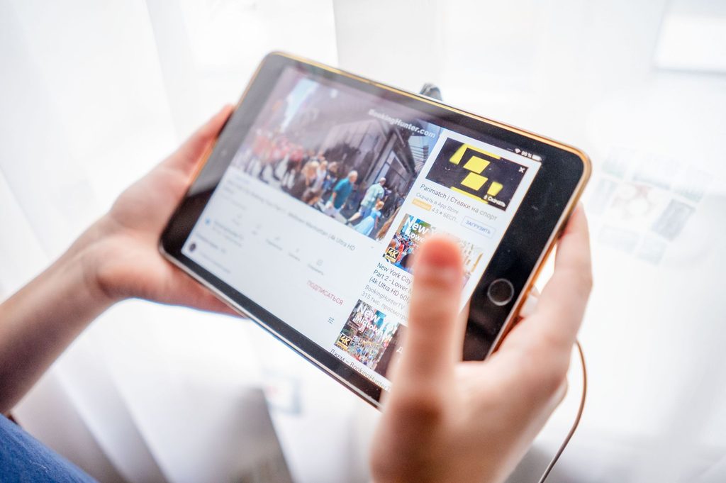 Close-up view of hands holding a tablet, displaying a digital video streaming platform.