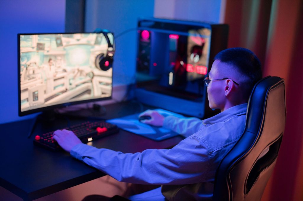  A person wearing glasses sits in a gaming chair, watching game streams and interacting with a PC setup.