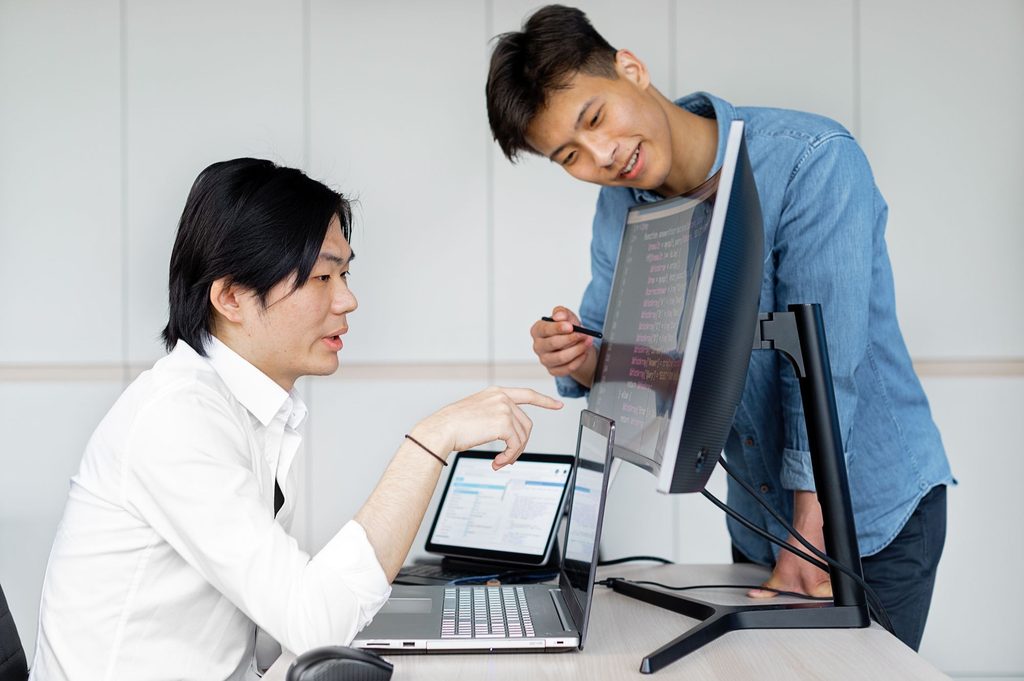 Two developers review code and interface elements on a computer screen for the Vietnamese market.