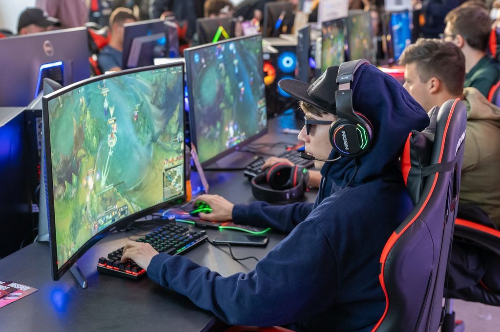 An esports player participates in a competitive match surrounded by other players at a gaming event.