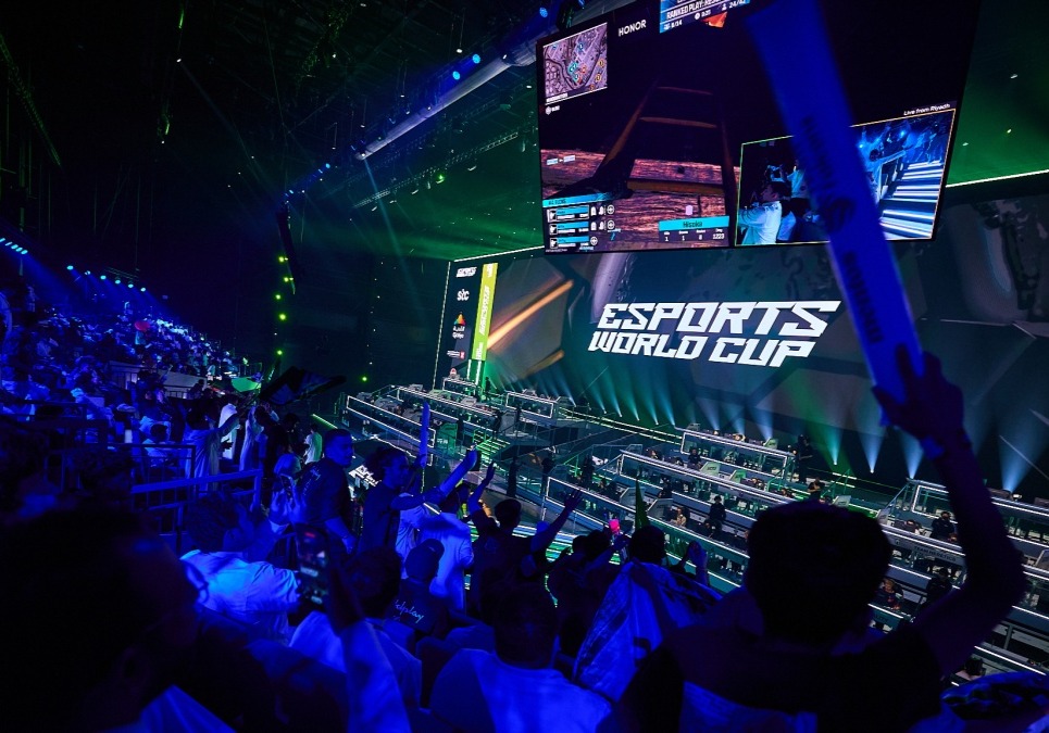 Audience cheering in the EWC 2026 arena with large screens displaying logo and gameplay.
